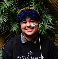 Mac - Young person with curly blue hair smiling. He has a feeding tube.