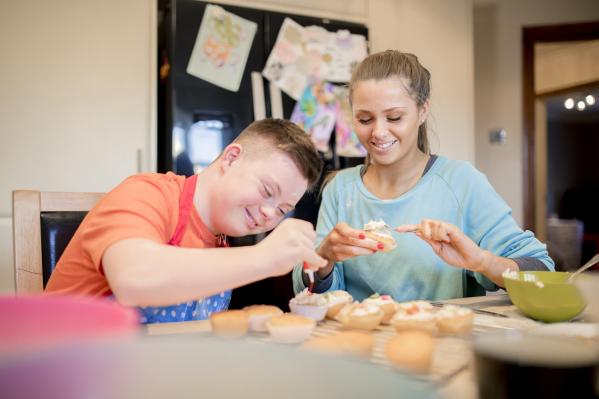 A teenager with Down syndrome next to a young women. They are baking.