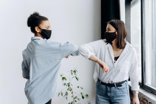 Two young people wearing masks are elbow bumping and smiling