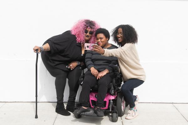 3 Black and disabled friends smiling and taking a cell phone selfie together.