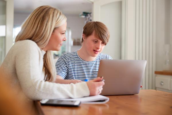 A young man with Down syndrome on a laptop with a woman sitting next to him