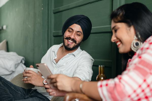 Happy expressive couple sip tea and look at phone