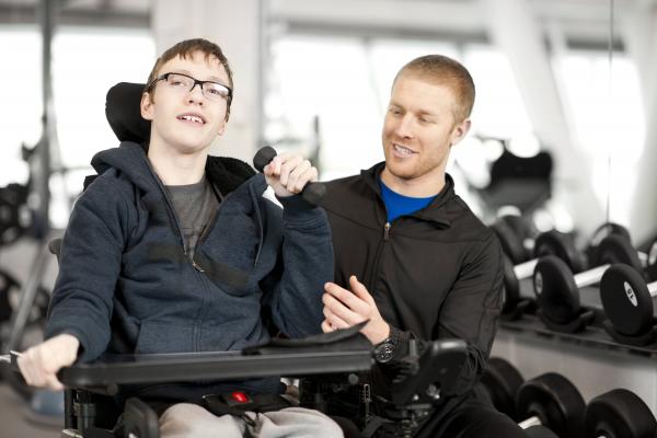 A teenage boy who uses a wheelchair sitting next to a man in a gym
