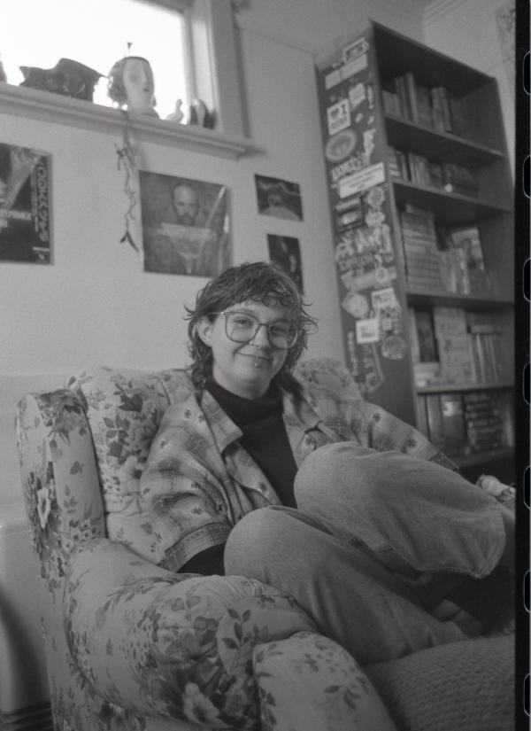 Is sitting on a couch smiling at the camera