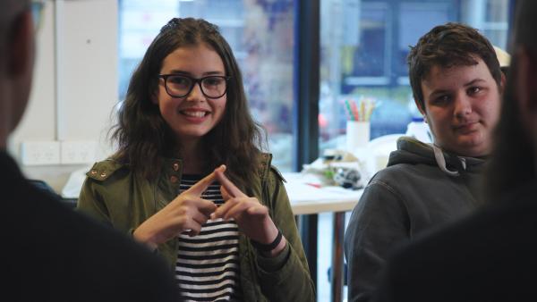 A young person who is Deaf using Auslan. She is smiling at the camera.