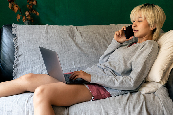 young person on couch with laptop and phone